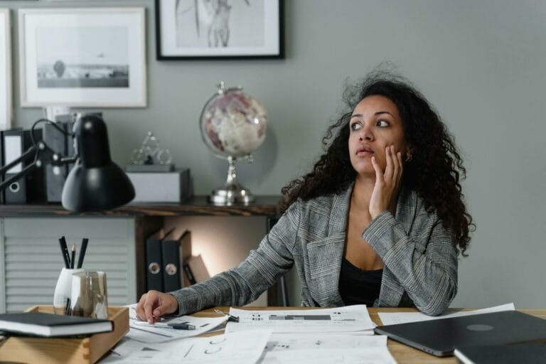 A Woman in Plaid Blazer Sitting Near the Table with Her Hand on Her Face