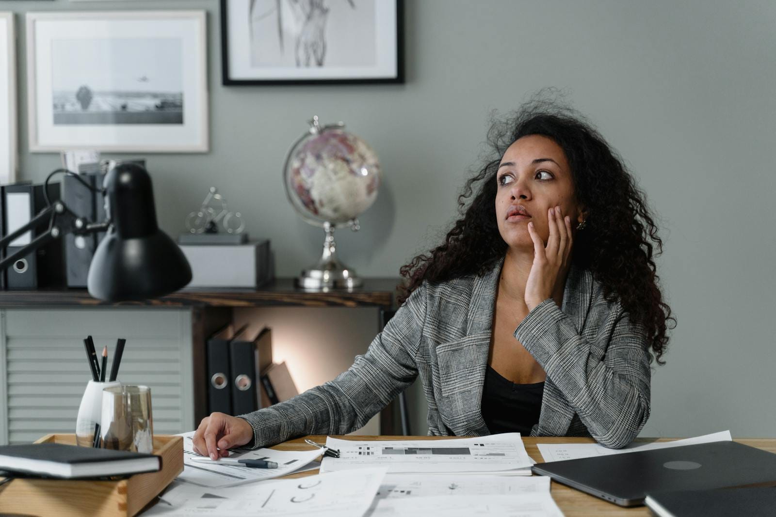 A Woman in Plaid Blazer Sitting Near the Table with Her Hand on Her Face